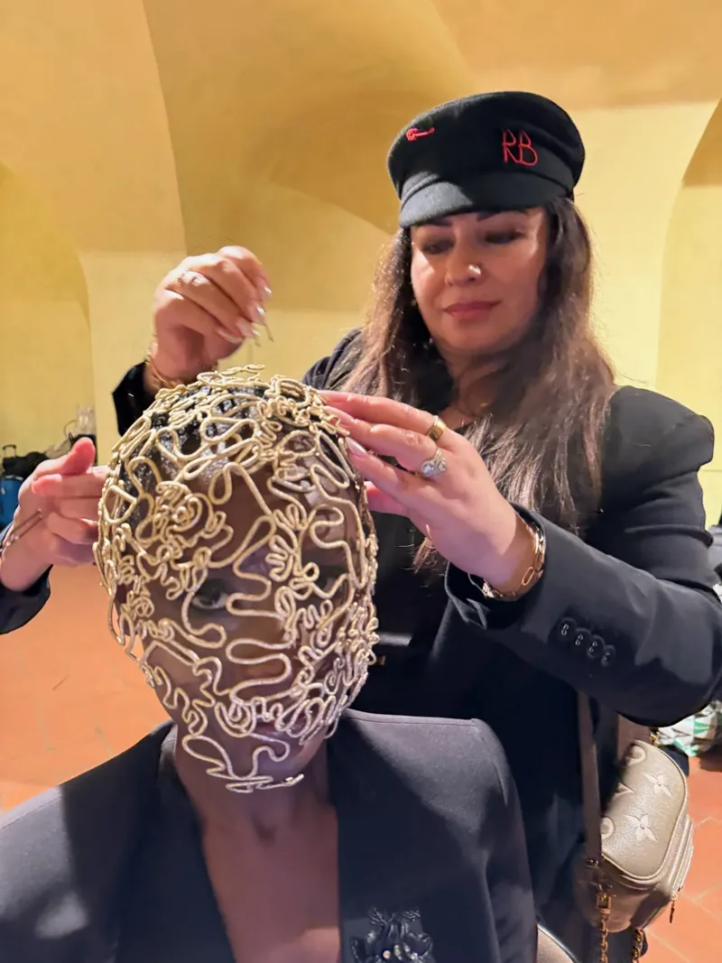 An AHA stylist fitting a sculptural gold headpiece on a model backstage